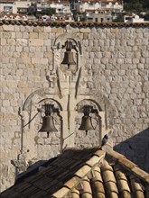 A bird sits on an old bell in a stone wall in the foreground with modern buildings in the