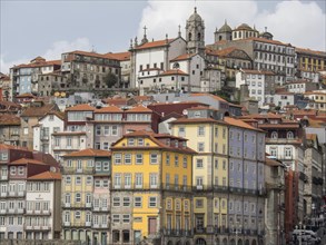 Many colourful buildings with orange roofs stretching up the hill, church towers and clouds in the