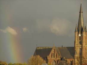 A gothic church with a high tower under a cloudy sky and a rainbow in the background, rainbow at a