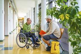 Full length photo of a man with disability talking with university colleague in the corridor