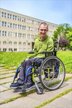Man in wheelchair smiling at camera outside the university in the campus with green grass