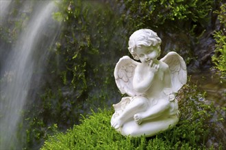 Porcelain angel figurine on moss by a waterfall