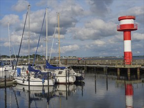 Harbour view with sailing boats, jetty and a red and white lighthouse, calm water and clouds in the