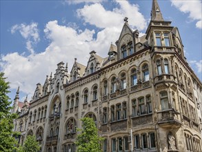 Two-storey building in neo-Gothic style with gabled towers and ornate windows under a cloudy sky,