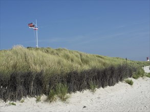 A flagpole stuck in grassy dunes under a clear blue sky on the beach, Heligoland, Germany, Europe