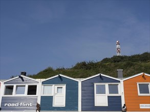 A row of colourful houses against a bright blue sky and a lighthouse on a hill in the distance,