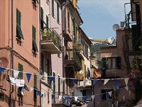 Colourful house facades with shutters and washing lines, above which hang pennants in an old town,