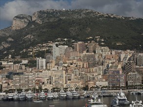 Large city with skyscrapers on a green hill and boats in the foreground under a cloudy sky, monaco