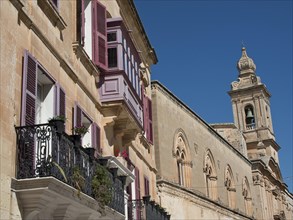 Row of historic buildings with balconies and shutters under a clear sky, the town of mdina on the