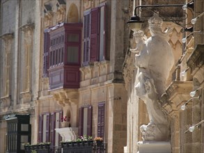 A building facade with colourful shutters, balconies and a statue, the town of mdina on the island