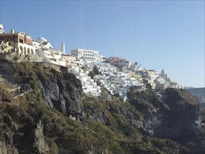 White houses on a hill with rocks by the sea under a clear sky in Greece, brown volcanic island in