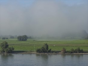Fog lies over green meadows and a river creating a peaceful atmosphere, ships on the rhine river in