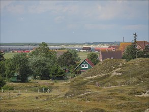 A wide view of a village with colourful houses in a hilly landscape near the sea, Baltrum Germany