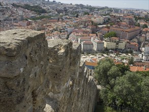 View from a fortress wall over the roofs of a city with many houses and green spaces, Lisbon,