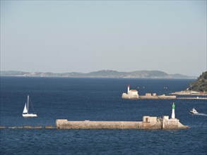 Lighthouse and sailing boat on the sea, small islands in the background under a clear sky, la seyne