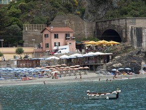 Beach and coastline with buildings and parasols, surrounded by rocky hills and clear water, Bari,