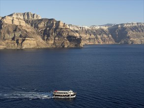 A boat sails along a peaceful, rocky coastline in clear waters, The volcanic island of Santorini