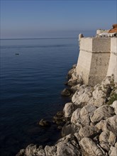 Stone wall along the quiet coast with cliffs and blue sea, the old town of Dubrovnik with historic