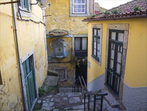 Narrow alley with yellow buildings, windows, doors and a staircase in an urban environment, old