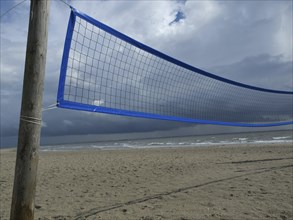 A volleyball net on the beach under a cloudy sky and slightly stormy weather with the sea in the