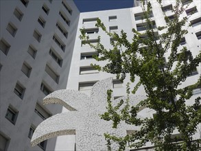 A tall, modern building near a large tree in summer, which is part of an urban complex, Lisbon,