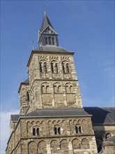 Romanesque church tower with stone masonry under a clear blue sky, Maastricht, Netherlands