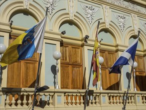 Various flags in front of the facades of a historic building with decorative lamps, tenerife, spain