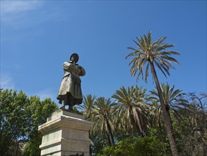 A statue raised against a blue sky and surrounded by palm trees, palermo in sicily with an