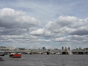 Summer cityscape with river and bridge, clouds floating above and a skyline in the background,