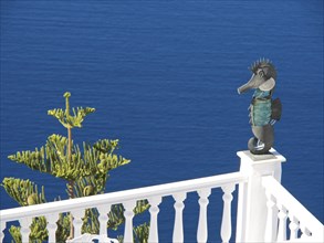 Seahorse sculpture on a railing in front of a deep blue sea and blue sky in Greece, The volcanic