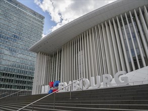 Modern building in Luxembourg with striking columns and glass facade, partly cloudy, modern