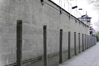 High concrete wall with wire mesh fence and security lighting. Gloomy, cold atmosphere,