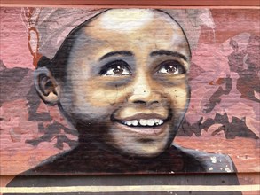 Street art mural showing a smiling face of a dark-skinned girl radiating hope, unknown artist,