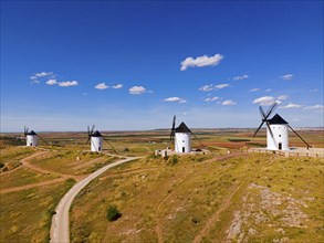 Four windmills stand on a hill under a bright blue sky in a vast summer landscape, aerial view,