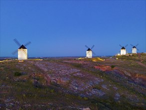 Several windmills on a hill at dusk in a wide field landscape under a clear sky, aerial view,