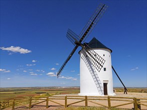 A windmill stands alone in a field under a bright blue sky in a vast summer landscape, aerial view,