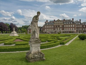 Stone sculpture in the foreground of a historic castle with decorative hedges and manicured garden,