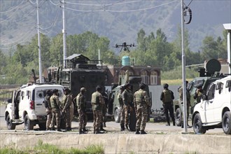 Military personnel standing near vehicles with equipment, conducting an operation in a mountainous