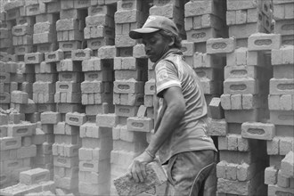 Man stacking bricks in an industrial setting with piles of bricks in the background, Jammu and