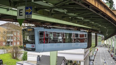 A suspension railway runs above a busy city street with cars and buildings in Wuppertal Vohwinkel