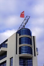 A modern office building with a round glass tower and a flag under a cloudy sky, Willy-Brandt-Haus,