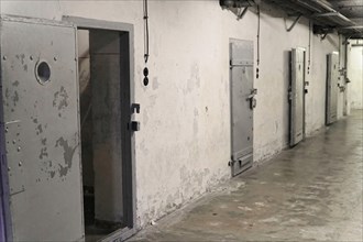 Prison corridor with several robust metal cell doors and light switches. Gloomy, deserted