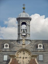 A clock tower with bells and a large clock on a historic castle building under a cloudy sky, old