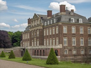 A magnificent historic brick castle, surrounded by green countryside and trees, under a blue sky,