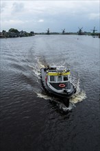 A Dutch boat travels across open water with windmills in the background. Zaan, Netherlands