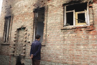 A man inspects a partially burnt and damaged brick building with broken windows, Encounter,