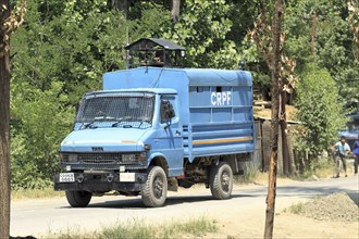 Blue police truck patrolling along a road lined with trees on a sunny day, Encounter, Pulwama,