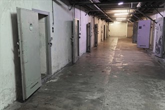 Long prison corridor with several open metal cell doors. Gloomy and deserted atmosphere,