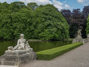 Several stone sculptures along a pond, surrounded by green trees and manicured hedges, old red