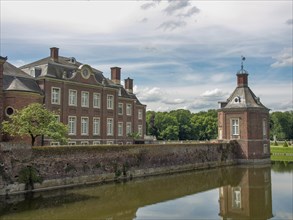 A historic castle with a moat in the foreground and a cloudy sky in the background, old red brick